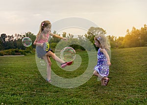 Two adorable little kids are playing with soap bubbles on the field.