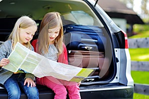 Two adorable little sisters exploring a map before going on vacations with their parents