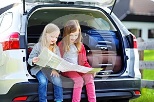 Two adorable little sisters exploring a map before going on vacations with their parents