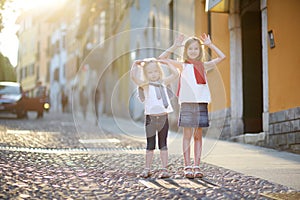 Two adorable little sisters having fun together on warm and sunny summer evening in Desenzano del Garda town, Italy