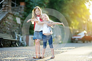 Two adorable little sisters having fun together on warm and sunny summer evening in Desenzano del Garda town, Italy