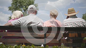 Two adorable mature couples sitting on the bench and talking together. Mature people resting outdoors. Cheerful senior