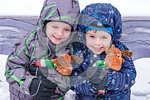 two adorable preschool kids brother boys in winter wear sit amoung snow and play with toy reindeer