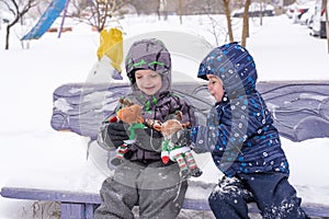 two adorable preschool kids brother boys in winter wear sit amoung snow and play with toy reindeer
