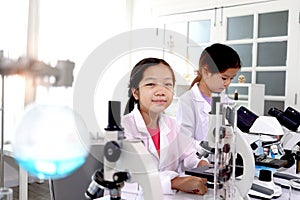 Two adorable pretty schoolgirls in lab coat doing simple science experiments, young Asian kid scientist having fun in chemistry