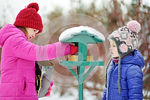 Two adorable sisters feeding birds on chilly winter day in city park. Children helping birds at winter.