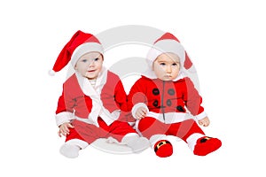 Two adorable young babies are sitting in santa claus suit and hat