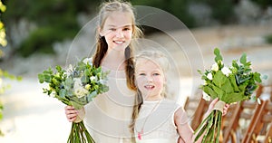 Two adorable young bridesmaids holding beautiful flower bouquets after wedding cemerony outdoors