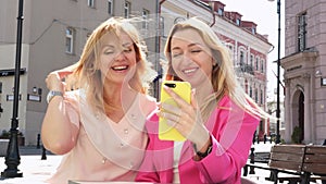 Two adult female friends are relaxing in a cafe in the city center and taking a selfie together.