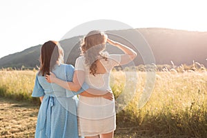 Two adult girlfriends hug each other at the background of nature