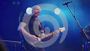 Two adult men play electric guitars at concert in club. Musicians perform on stage