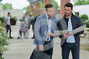 two adult men on university campus looking at folder