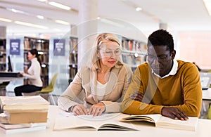 Two adult students studying together in public library