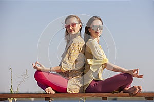Two adult women aged yoga outdoors in summer in the park