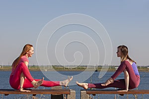 Two adult women aged yoga outdoors in summer in the park
