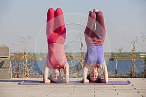 Two adult women aged yoga outdoors in summer in the park