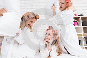 Two adult women and a girl play a fight with pillows on the bed.