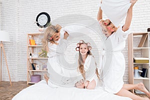 Two adult women and a girl play a fight with pillows on the bed.