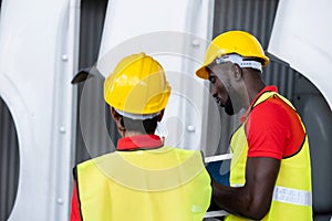 Two African America engineer wearing safety helmet and vest standing in the automotive warehouse with blur background. Man holding