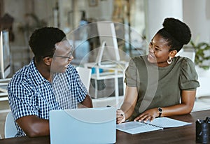 Two african american businesspeople having a meeting and looking at a report while working on a laptop together at work
