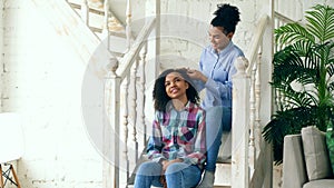 Two african american curly girls sistres make fun curly hairstyle each other and have fun at home