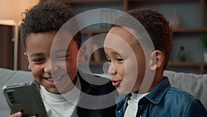 Two African American little boys brothers laughing browsing mobile phone without parents bad behavior young generation