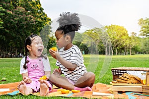 Two African American little girl sitting on the mat and eating oranges fruits in the autumn park , play with oranges fruits