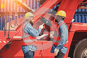 Two African American logistic workers wearing reflective vests and white helmets talk about logistics operations at shipping