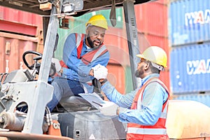 Two African American males in safety uniforms and helmets, container operating working with the forklift truck driver at