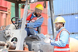 Two African American males in safety uniforms and helmets, container operating working with the forklift truck driver at