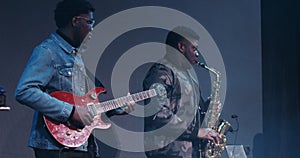 Two African American men play musical instruments while standing on the stage