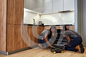 Two African American repairpersons in front of opened kitchen oven