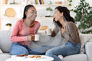 Two african besties laughing while drinking tea together at home