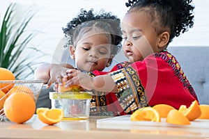 Two African cute kid girls squeezing fresh oranges at home. Adorable children siblings help making freshly squeezed orange juice