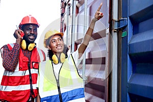 Two African engineer man and woman wearing safety vest and helmet working together at logistic shipping cargo container yard,