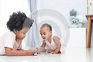 Two African kids, cute newborn 11 months baby girl and 5 years old boy, brother and sister playing together on floor, having fun