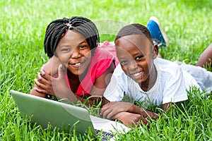 Two african kids laying on grass with laptop.
