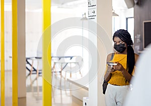 Two african students with mask using their mobile phones on campus