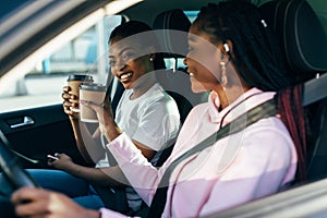 Two african woman drinkink coffee to go in the car while driving car on the travel