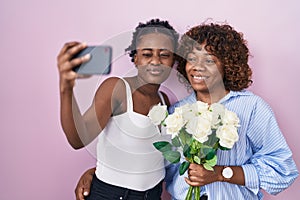 Two african women taking a selfie photo with flowers winking looking at the camera with sexy expression, cheerful and happy face