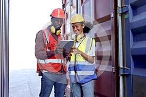 Two African workers wear safety vest and helmet at logistic shipping cargo containers yard. Happy young engineer woman uses