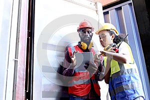 Two African workers wear safety vest and helmet at logistic shipping cargo containers yard. Happy young engineer woman uses