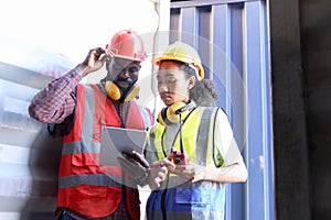 Two African workers wear safety vest and helmet at logistic shipping cargo containers yard. Happy young engineer woman uses