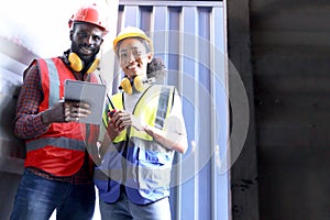 Two African workers wear safety vest and helmet at logistic shipping cargo containers yard. Happy young engineer woman uses