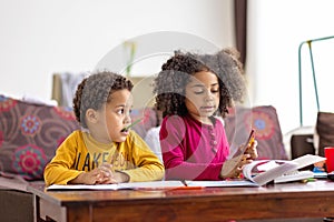 Two afro american kids sititng at home spending qulity time together,  drawing writing reading