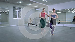 Two agile slim ballerinas rehearsing simultaneous steps pirouette with ballet dancers warming up at background in dance