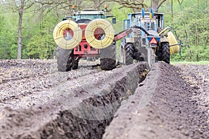 Two agriculture tractors digging drainage pipes in ground