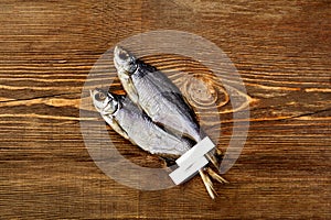 Two air-dried silver breams with labels on tails on wooden table surface