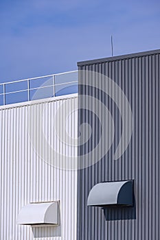 Two air ducts ventilation on grey and white corrugated metal factory buildings wall with blue sky background