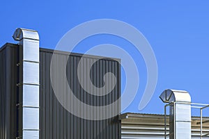 Two air ventilation ducts outside of modern industrial building against blue sky